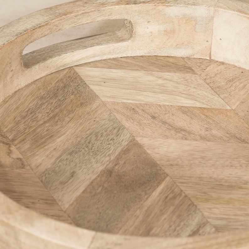 May include: A round wooden tray with a herringbone pattern and a handle. The tray is made of natural wood and has a light brown color.