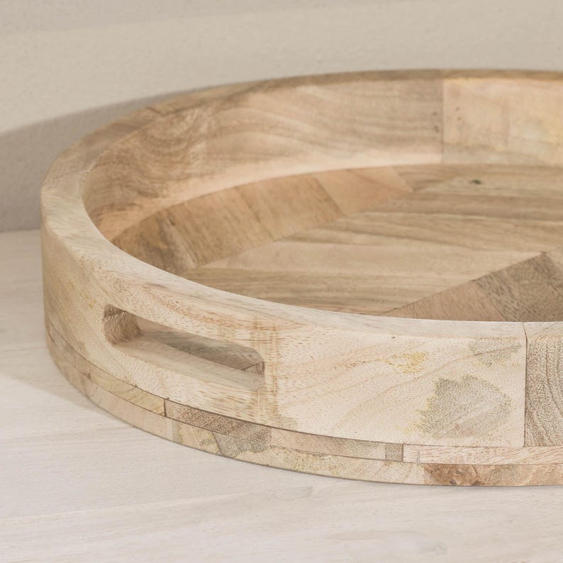 May include: A round wooden serving tray with a natural wood finish and a geometric pattern. The tray has a built-in handle.