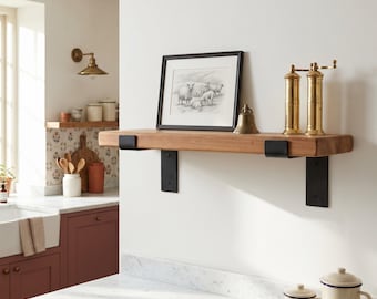 Puede incluir: Un estante flotante de madera natural montado con dos soportes de metal negro. Sobre el estante hay un boceto en blanco y negro enmarcado de ovejas, una pequeña campana de latón y dos molinillos de pimienta altos de latón.