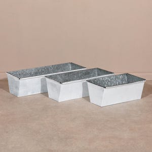 Può includere: Tre fioriere rettangolari in metallo zincato di varie dimensioni. Le fioriere hanno una finitura argentata e un design semplice e industriale. Sono adatte per uso interno o esterno.