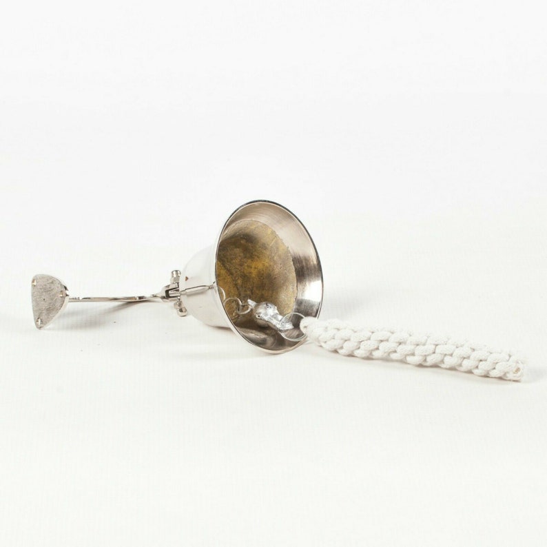 May include: A silver-colored oil lamp with a white wick. The lamp has a bell-shaped top and a small, flat handle. The wick is made of a thick, braided cotton material.