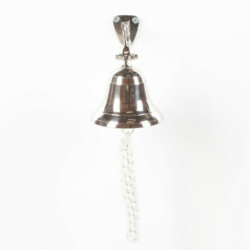 May include: A polished silver bell with a white rope pull, mounted on a silver bracket. The bell is suspended against a white background, showcasing its reflective surface and nautical design.