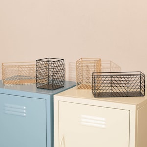 May include: Three wire mesh storage baskets in black and gold. The baskets are sitting on top of two blue and white metal cabinets.