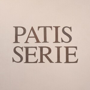 May include: A sign with the words "PATISSERIE" in brown letters on a light pink background.