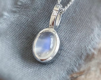 May include: A silver necklace with a moonstone pendant and small diamond accents. The pendant is oval shaped and has a light blue iridescent sheen.