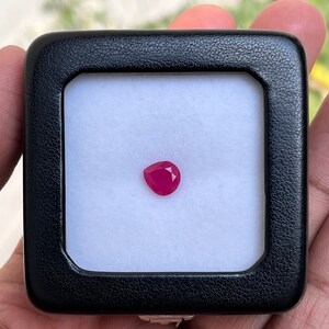 Puede incluir: Una piedra preciosa rosa en una pequeña caja negra con interior blanco.