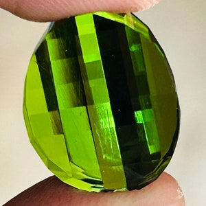 May include: A green gemstone with a faceted cut. The gemstone has a dark green color with lighter green stripes.