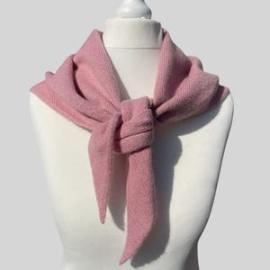 Könnte beinhalten: Ein weicher rosa gestrickter Schal, der um den Hals einer weißen Puppe gebunden ist. Der Schal ist aus feinem Strick und hat einen zarten Fall.