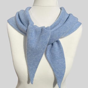 May include: A light blue knitted scarf tied in a knot around a white mannequin's neck. The scarf is made of a soft, lightweight material and has a simple, elegant design.