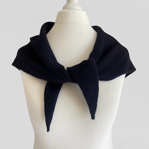 May include: A dark blue knitted scarf with a simple, elegant design. The scarf is tied in a knot at the front and drapes over the shoulders.