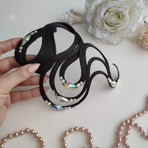 May include: A black hair accessory featuring a series of curved, wave-like strands adorned with iridescent, multi-faceted crystals. The structure is composed of smooth, dark material arranged in an abstract, flowing pattern with clear, sparkling accents.