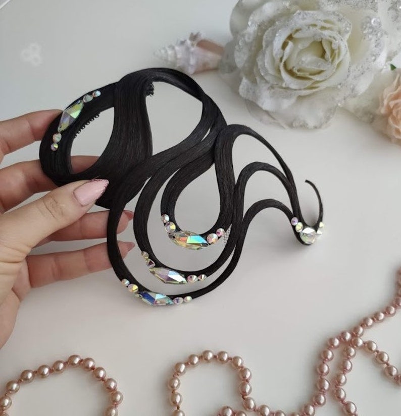 May include: A black hair accessory featuring a series of curved, wave-like strands adorned with iridescent, multi-faceted crystals. The structure is composed of smooth, dark material arranged in an abstract, flowing pattern with clear, sparkling accents.