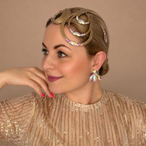 May include: A hair accessory featuring light brown hair styled in intricate loops adorned with iridescent, multi-faceted crystals. The accessory is paired with matching crystal stud earrings that feature a cluster of marquise-cut stones.