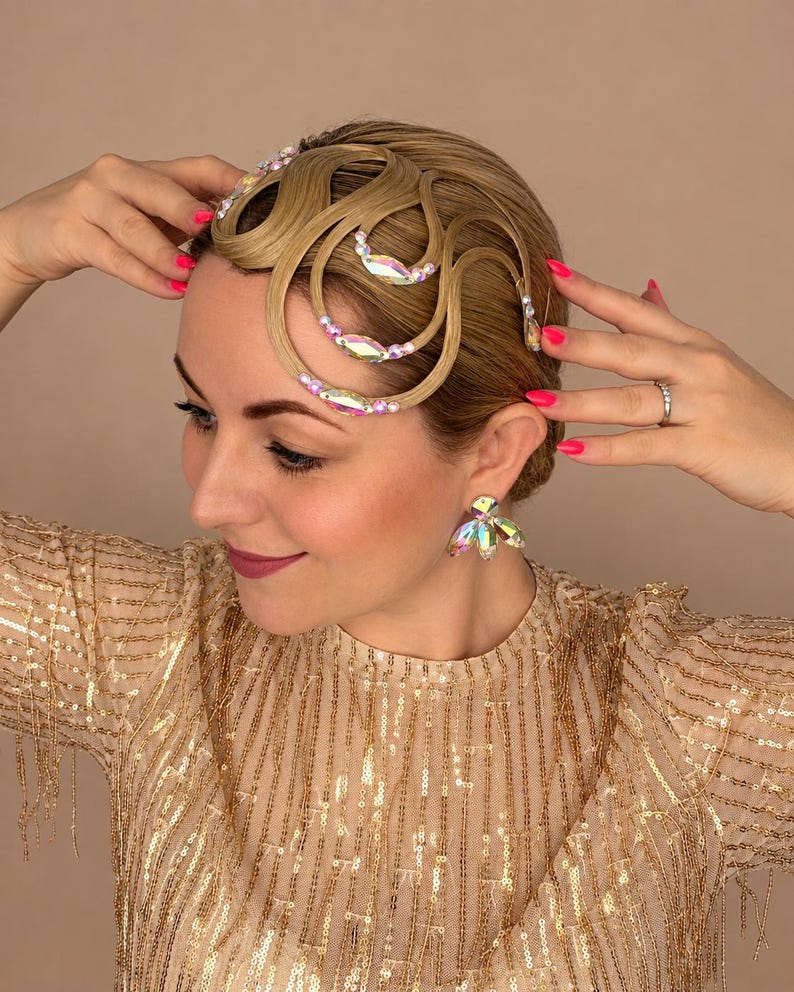 May include: A blonde hair accessory featuring intricate, curved, wave-like hair sections adorned with iridescent, multi-faceted crystals and small white beads. The accessory is paired with matching crystal-embellished earrings in a floral shape.