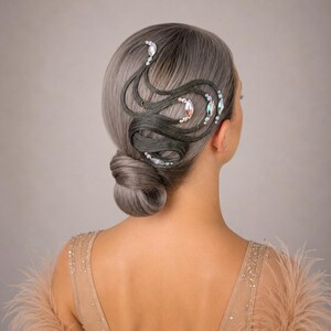 May include: A low bun hairstyle featuring silver-grey hair styled with intricate, swirling dark grey hair extensions. The design is accented with iridescent marquise-shaped crystals and small white pearls arranged in curved patterns along the side.
