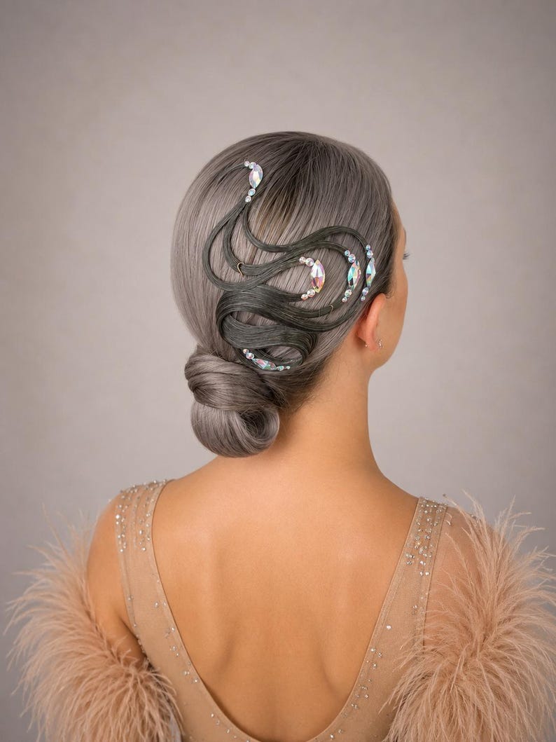 May include: A low bun hairstyle featuring silver-grey hair styled with intricate, swirling dark grey hair extensions. The design is accented with iridescent marquise-shaped crystals and small white pearls arranged in curved patterns along the side.