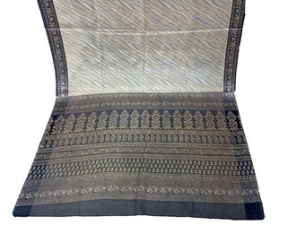 May include: A white and grey patterned saree with a black and gold border. The border features intricate floral and geometric designs.