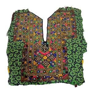 Può includere: Un collo ricamato colorato con un motivo geometrico e decorazioni a specchio. Il collo è su un tessuto verde con un motivo floreale.