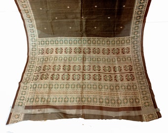 May include: A brown and beige patterned saree with a geometric design. The saree has a thin, transparent border.