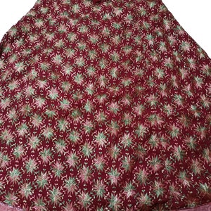 May include: A maroon fabric skirt with a floral pattern in shades of green, pink, and gold. The skirt has a gathered waist and a flowing silhouette.