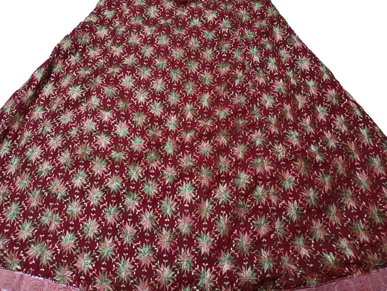 May include: A maroon fabric skirt with a floral pattern in shades of green, pink, and gold. The skirt has a gathered waist and a flowing silhouette.