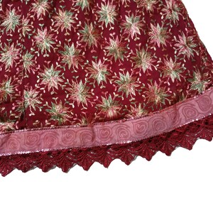 May include: A burgundy skirt with a pink and gold floral embroidered pattern. The skirt has a pink ribbon trim and a burgundy lace trim.