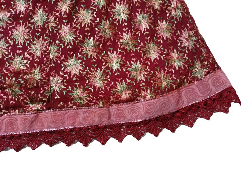 May include: A burgundy skirt with a pink and gold floral embroidered pattern. The skirt has a pink ribbon trim and a burgundy lace trim.