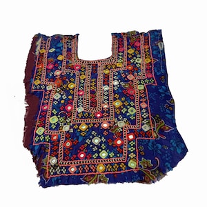 Puede incluir: Una blusa azul bordada con intrincados espejos y trabajo de hilo. La prenda presenta un escote cuadrado y está adornada con coloridos estampados florales y geométricos. Los bordes tienen un ribete con flecos.