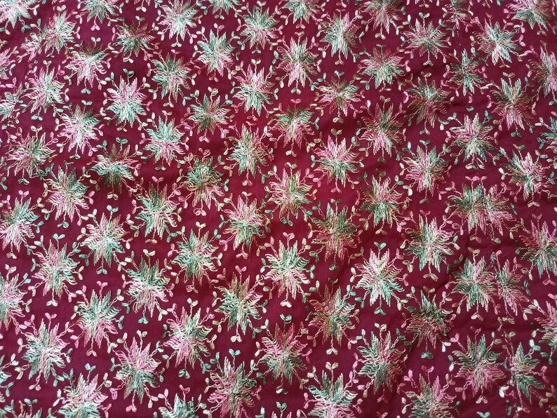 May include: Burgundy fabric with a repeating pattern of embroidered flowers in shades of pink, green, and gold.
