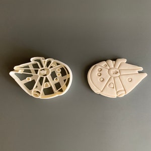 May include: Two white plastic cookie cutters shaped like the Millennium Falcon spaceship from Star Wars.