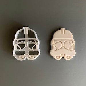 Puede incluir: Un cortador de galletas de plástico blanco con forma de casco de soldado clon de Star Wars. El cortador se muestra de frente y está listo para usarse para cortar masa de galletas.