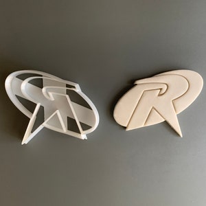 May include: Two white plastic cookie cutters shaped like the Robin logo. The logo is a stylised letter "R" with a star inside a circle.