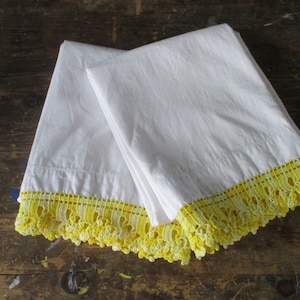 May include: Two white pillowcases with yellow crocheted lace trim. The lace trim is a delicate pattern with a scalloped edge.