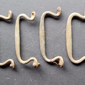 May include: Six antique metal drawer pulls. The pulls are a weathered brass colour, with a C-shaped handle and decorative curled ends. Each pull has two mounting holes. The pulls are made of metal.