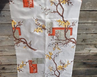 May include: A beige fabric with a repeating pattern of brown branches with yellow and white flowers. The fabric also has a geometric pattern of orange and green squares.