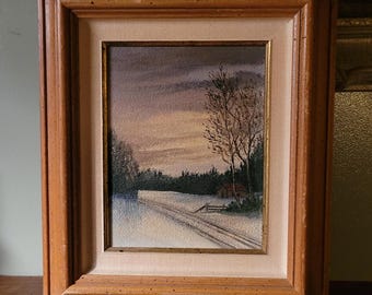 May include: A framed painting of a winter scene with a small cabin in the distance. The painting is done in muted tones of blue, gray, and white, with a hint of pink in the sky. The painting is framed in a simple wooden frame.