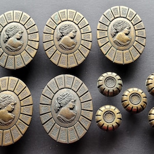 May include: A collection of antique bronze-toned cabinet knobs and pulls. The larger oval knobs feature a classical cameo design of a woman's profile within a sunburst frame. Smaller round knobs are also included.