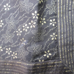 Peut inclure: Gros plan sur un tissu noir avec un motif floral doré. Le tissu a une bordure dorée avec des rayures.