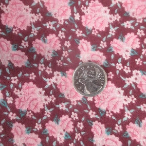 May include: Close-up of floral fabric with a burgundy background and pink roses. Small white flowers and teal leaves are scattered throughout the design. A quarter coin is in the image for scale.