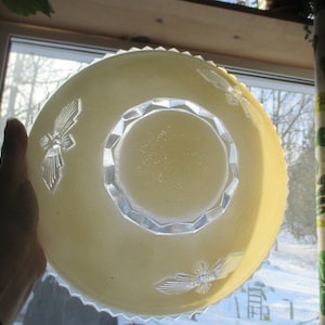 May include: A clear glass bowl with a scalloped edge and a raised, geometric design in the centre. The bowl has a pale yellow tint and features two butterfly designs on the sides.