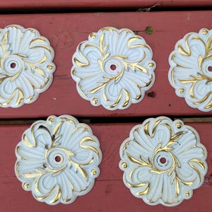 May include: Five white ceiling medallions with gold leaf accents. Each medallion has a circular design with a central hole.