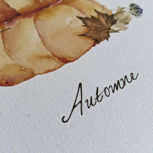 May include: Watercolor painting of two pumpkins with a brown maple leaf and a purple flower. The word "Automne" is written in cursive below the pumpkins.