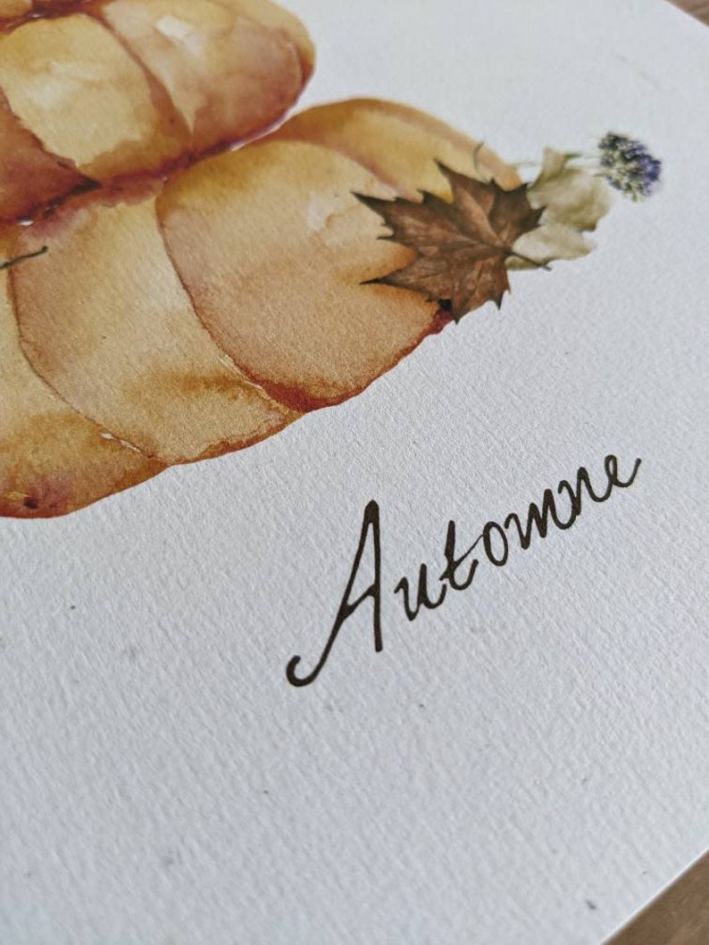 May include: Watercolor painting of two pumpkins with a brown maple leaf and a purple flower. The word "Automne" is written in cursive below the pumpkins.