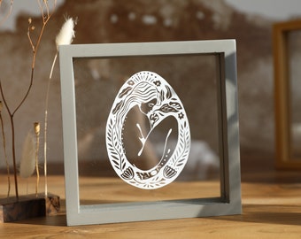 Birth of a woman, small square frame in transparent gray wood to put or hang on the wall, paper cut between 2 glasses
