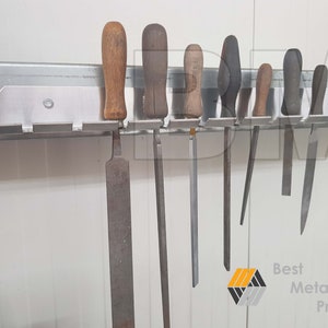 May include: A metal wall-mounted tool holder with eight slots, holding various metal files with wooden handles. The holder is silver and the files are a mix of silver and black.