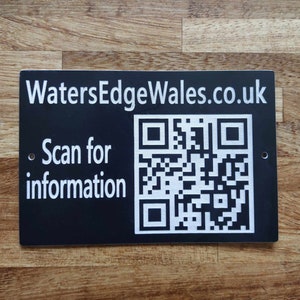May include: Black rectangular sign with white text and a QR code. The text reads "WatersEdgeWales.co.uk" and "Scan for information".