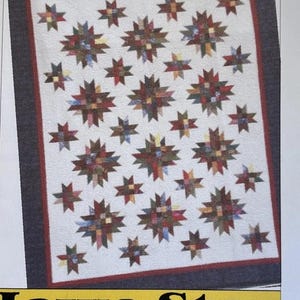 May include: A quilt pattern titled Galaxy by Iowa Star Designs, 534 2nd Street, Traer, IA 50675 319.478.2738. The quilt features a white background with a dark border and numerous multi-colored star motifs in various sizes arranged across the surface.