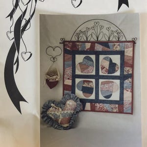 May include: A sewing pattern titled Country Heartstrings and Crazy Hearts featuring a 23-inch wall hanging with four heart blocks, a heart-shaped pillow with ruffled edges, and a small heart ornament hanging from a wire stand with a bow.
