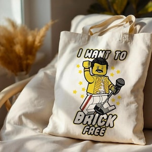 May include: A cream-colored canvas tote bag featuring a graphic of a yellow plastic toy figure dressed in a yellow jacket and white pants, holding a microphone. The text "I WANT TO BRICK FREE" is printed in black above and below the figure.