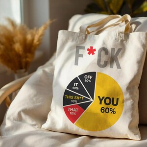 Könnte beinhalten: Eine cremefarbene Stofftasche mit dem grauen Schriftzug F*CK und einer großen Tortengrafik. Die Segmente sind beschriftet mit IT 10%, OFF 10%, THIS SH*T 10%, THAT 10% und einem großen gelben Bereich mit der schwarzen Aufschrift YOU 60%.